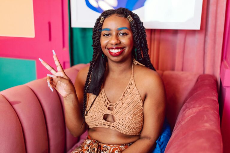 Vibrant portrait of a smiling woman sitting indoors showing a peace sign.